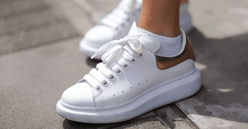Close-up of white Alexander McQueen Oversized sneakers with a black heel tab, worn on a paved street