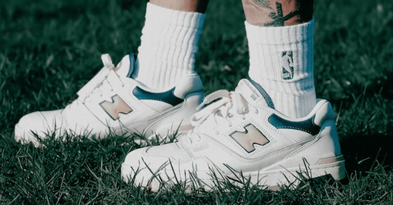 White New Balance 550 sneakers with green and grey details, worn with white socks on grass
