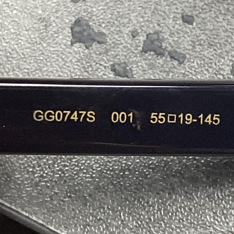 La parte interior de una patilla negra de gafas de sol Gucci impresa en dorado con GG0747S 001 55□19-145: el modelo, la combinación de colores y el ancho de lente, el puente y el largo de la patilla