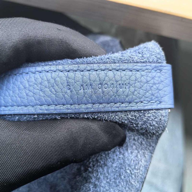 Hermès blind stamp embossed on a blue leather bag strap, showing the year letter alongside the craftsman characters