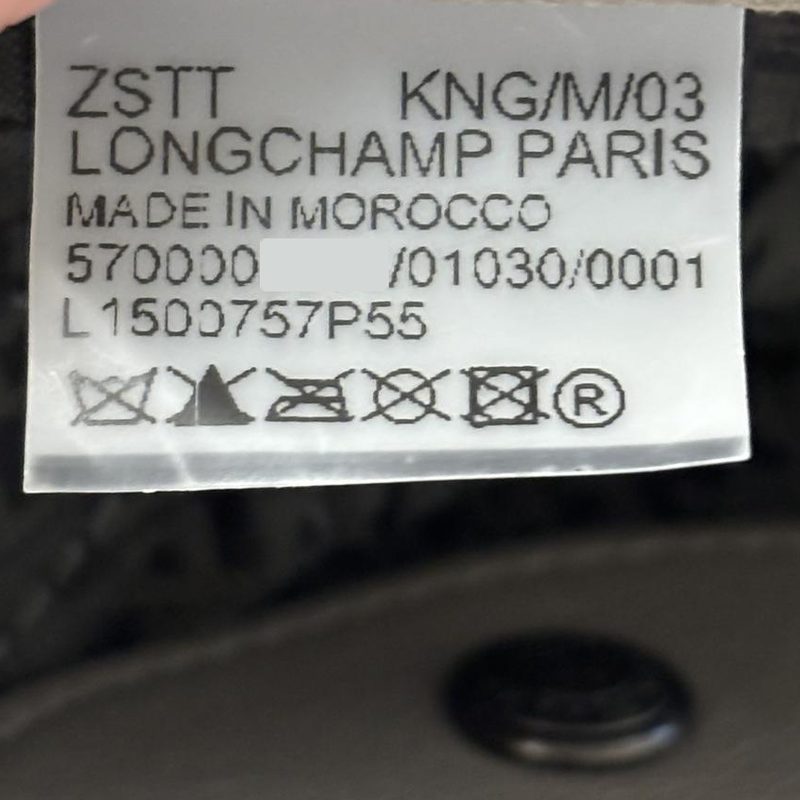 Una etiqueta transparente de Longchamp dentro de un bolso de asa superior Le Pliage Cuir XS, con la referencia L1500757P55 en la última línea de texto, encima de los símbolos de cuidado