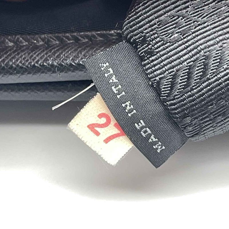A Prada woven label reading originality certified with its number, photographed upside down